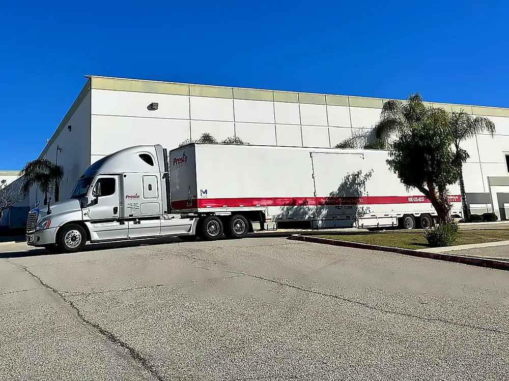 Presto Logistics tractor and moving trailer parked beside a large warehouse building