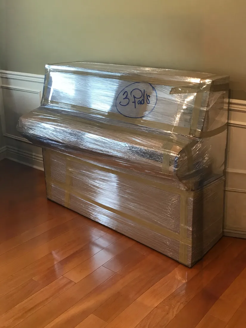 A wrapped upright piano, padded and ready to move